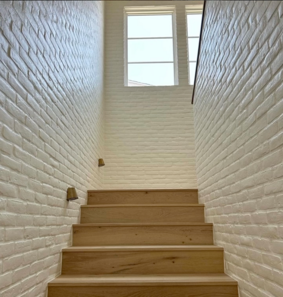 Natural wood staircase with Creative Mines Loft Paintgrade Brick Veneer walls painted in white.